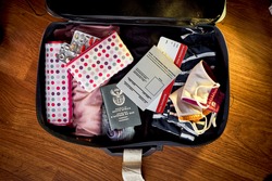 An image of a packed suit case on a wooden floor of a South African woman who has received her covid vaccine and has a certified travel certificate along with her passport and flight boarding pass