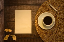 Blank paper card on rustic wooden background and cup of coffee on sisal or jute. Blank invitation to insert text. Top view.