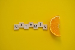 Word vitamin c in wooden letters on citrus yellow background. Concept of prevention against colds and antioxidant vitamin. Fresh orange slice.