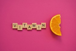 Word vitamin c in wooden letters on c hot pink background. Concept of prevention against colds and antioxidant vitamin. Fresh orange slice.