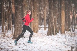 Winter running exercise. Runner jogging in snow. Young woman fitness model running in a city park 