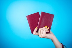 Womans hand holding a two red passports against blue background