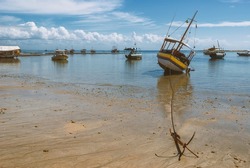 Morro de Sao Paulo, Bahia, Brazil. Fishing boat moored on the beach. Early in the morning on the second beach of the village. Low tide, blue sky with white clouds and reflection in the water.