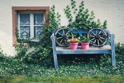 Old blue decoration bench with two wooden wagon wheels and two pink flower pots in the backyard