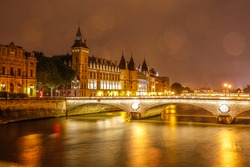 Conciergerie Building in Paris, France at night with lights reflection in the Seine River water in the running day