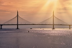 Cable - stayed bridge over the bay in the rays of the sun .  Waterscape at sunset .