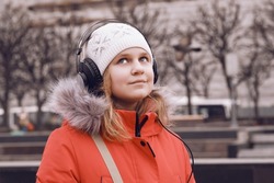 Girl 10-12 years old in outerwear listens to music. Child in headphones listening to the radio outdoors.