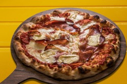 Pizza with  bacon or speck and brie cheese and tomato souce. Typical Italian product on wooden cutting board over yellow background