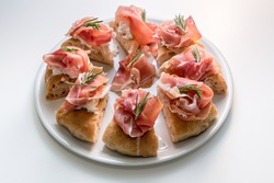 gourmet focaccia with prosciutto of Parma ham, mozzarella and rosemary sprigs, eight tasty slices of pizza on a white plate