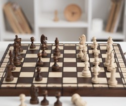 Chess pieces are laid out on a chessboard. A chess game in the heat of the battle. Brown chess pieces made of natural wood
