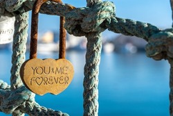 Close-up of a heart-shaped rust padlock with the inscription -You and Me Forever-