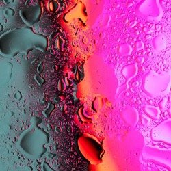 A macro shot of mixed drops of oil and water on a glass surface illuminated by bright neon light in color gradation. Abstract vivid bold colors background.