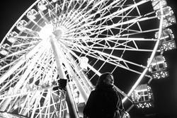 Young beautiful caucasian brunette woman posing by ferris wheel at night. Black and white photos