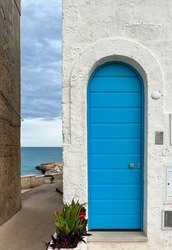 Closed and arched blue colored entrance door with white wall and succulents near the coastline