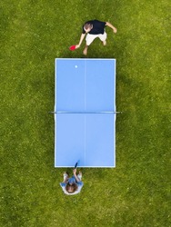 Aerial view people playing ping pong match outdoor. Top view two boys playing table tennis (pingpong) on a green grass lawn. Aerial view outdoor sport
