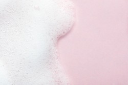 Foaming liquid on pink backdrop. Cosmetics foam background with copy space in right side. Cosmetic product sample of mousse, shampoo or soap. Skincare, cosmetology and beauty concept