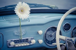 Retro styled image of an old car radio inside a blue pastel classic car, detail on the radio of a vintage car with white flower, Holiday vacation trip adventure concept.