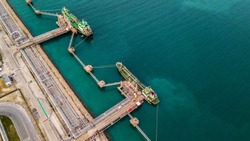 Aerial view two tanker ship loading in port, tanker ship under cargo operations on typical shore station with clearly visible mechanical loading arms and pipeline infrastructure. 