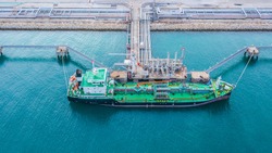 Aerial view of oil tanker ship loading in port, Oil tanker ship under cargo operations on typical shore station with clearly visible mechanical loading arms and pipeline infrastructure. 