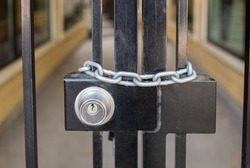 Lock and strong steel chain wrapped around the metal entrance gate. Closed metal gate with lock. Street photo, selective focus, nobody