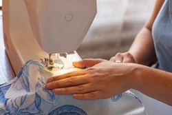 Sewing hands. Female hands stitching fabric on a machine hobby at home. Blurred background. Close-up. Freelancer working from home