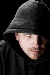 Dark low key portrait of a man looking at camera with a serious facial expression, wearing gray hood