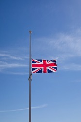 Portrait shot, Union Jack flag flying at half mast against blue sky representing national mourning or event