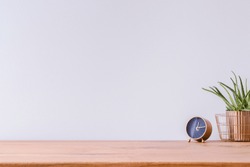 Photo of wooden home office desk with black and gold clock and fresh green plant against white empty wall