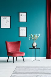 Paintings on the green wall in living room interior with red armchair and black side table with a flower vase on top