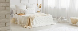 White bedroom interior with windows, gold accessories and white bedsheets on king-size bed