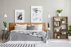 Patterned blanket on wooden bed between tables with plants in bedroom interior with posters. Real photo