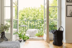 Real photo of open door to balcony with many fresh plants, lights, material pouf and view on urban jungle