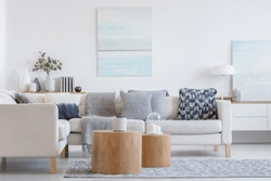 Two wooden coffee tables with plant in pot in front of grey corner sofa in fashionable living room interior