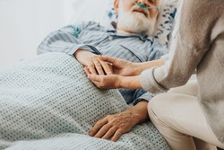 Close-up of older dying man holding his wife's hands