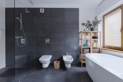 Glass floor shower in modern black bathroom interior with travertine walls in wellness spa center