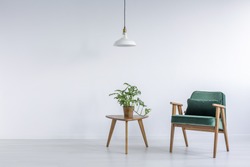 White room with green armchair, small table and plant