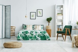 White bedroom with screen, bed, armchair, bookcase, lamp and pouf