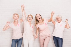 Group of smiling ladies with pink ribbons cheering and holding hands