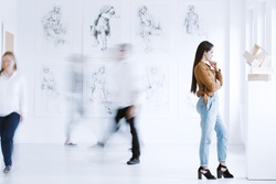 Young woman observing sculpture in modern art gallery with drawings. Art gallery concept 