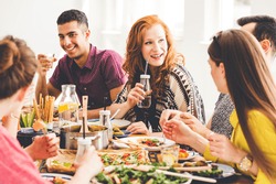 Group of mixed-race people celebrating vegan party at home, sitting at colorful table full of healthy snacks, salads and organic dishes