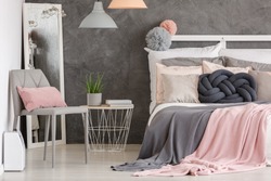 Pink pillow on grey modern chair in woman bedroom with pastel colored bedsheets on bed