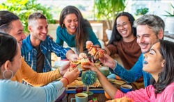multiethnic large group of friends sitting on cafe table restaurant eating a muffin making faces. diverse people celerating sweet breakfast together enjoying happy holidays. lifestyle and joy concept