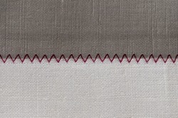 white and grey fabric stitched with a zigzag purple thread. Stitched pieces of fabric close-up. zigzag stitch.