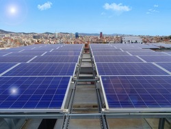 front view of solar panels on a rooftop overlooking the Barcelona skyline on a sunny day with a blue sky and solar glare effects