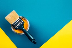 Brush on open can of yellow color paint on yellow and blue background. Flat lay style. Renovation concept.