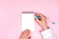 Woman's hands with perfect manicure holding pencil and spiral notepad as mockup for your design. Pink background, flat lay style.