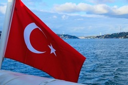 Turkish Flag in the wind. Blurred cityscape of Istanbul and Bosporus (Bosphorus or Strait of Istanbul). White crescent and a star on a red background.