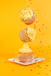 Vanilla cupcakes with yellow frosting and rainbow sprinkles floating on a yellow background