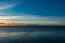 A sky with haze turning into cloudy on the horizon, during the white nights at sunset over a calm sea with fine ripples.