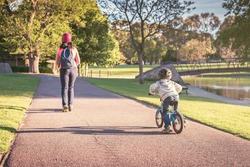 Litle boy riding his balance bike while following his mother in Adelaide Park Lands on a day